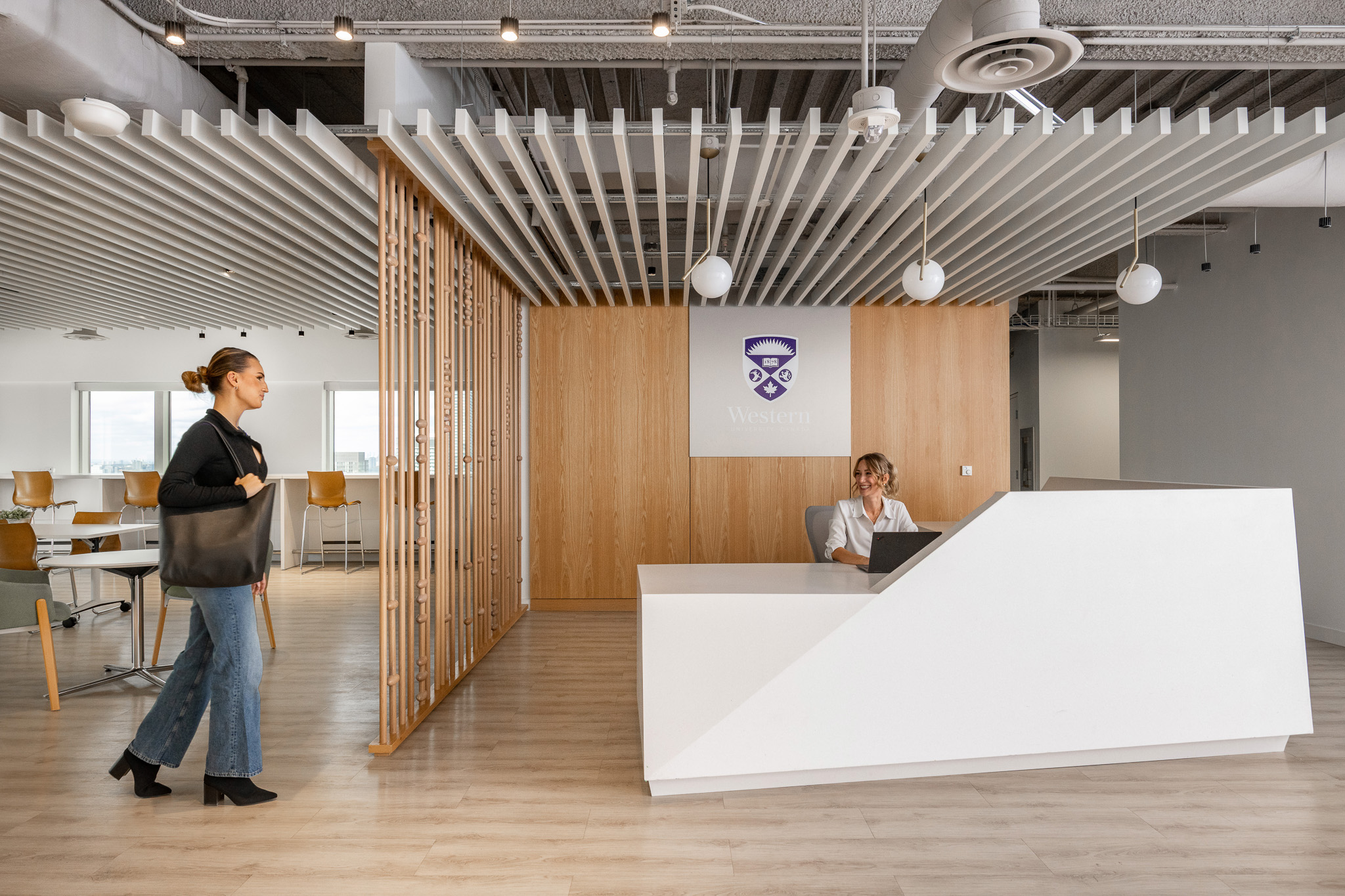 Reception area with a modern white desk, wooden accent wall displaying Western University logo and seating area with tables and chairs in the background.